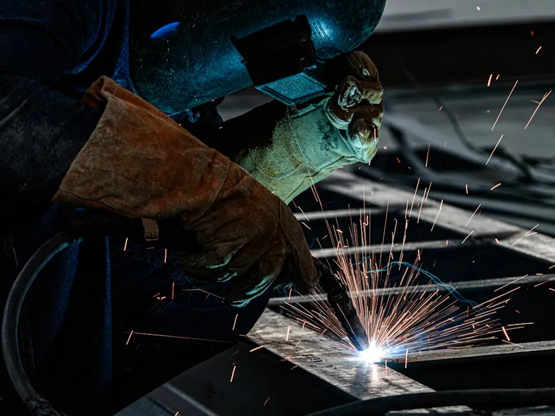 Juru las bekerja pada logam dengan percikan api di bengkel industri
