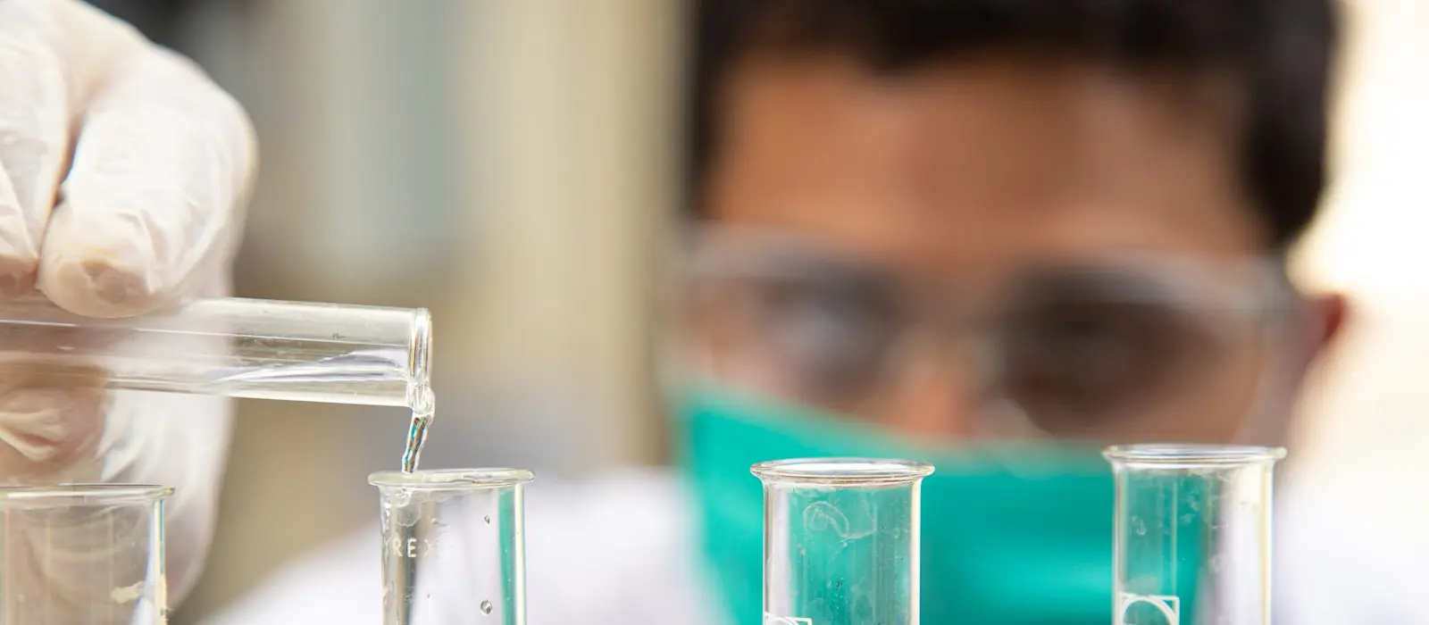 Petugas laboratorium bekerja di meja uji dengan alat pelindung diri lengkap